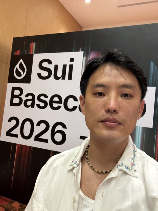 A man wearing a beaded necklace stands in front of a 'Sui Basecamp 2026' banner.