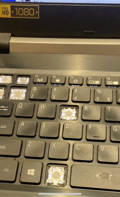 A close-up of a laptop keyboard with several keys removed, showing the internal key switch mechanisms, with a Full HD 1080 display visible above.