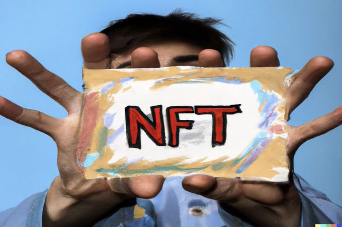A person holds up a colorful painted sign reading 'NFT' in bold red letters, obscuring their face against a blue sky background.
