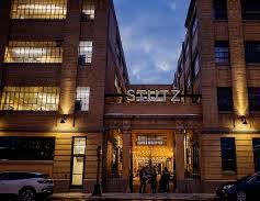 An illuminated brick building entrance bears the sign 'STEELZ' above its open doors at dusk.