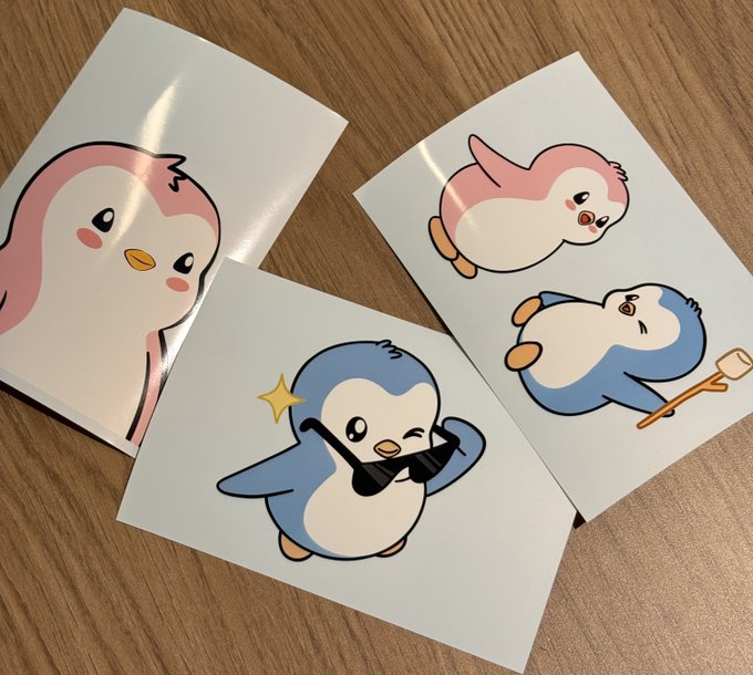 Three cute cartoon penguin stickers in pink and blue designs laid on a wooden surface.