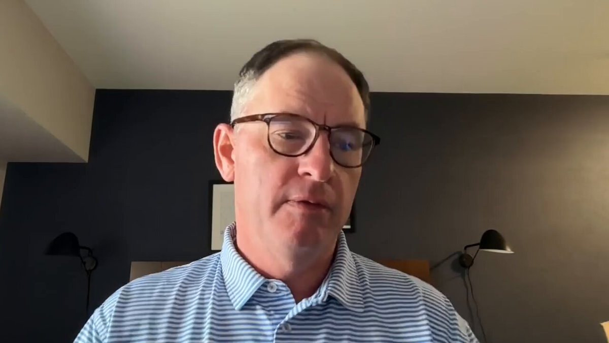 The image shows a man wearing glasses, looking down at something with a serious expression. He appears to be engaged in an online video call or watching a video on YouTube. The caption below the image provides information about the source of the content being viewed by the viewer.