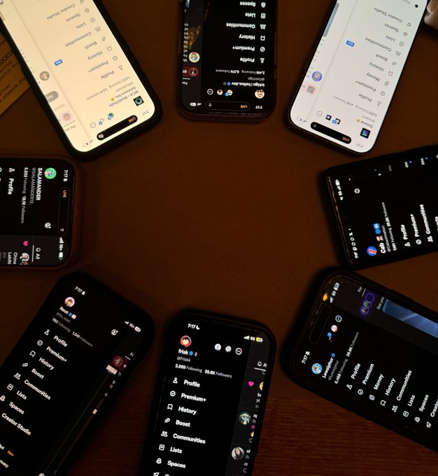 Multiple smartphones arranged in a circle on a wooden surface, all displaying the Twitter/X interface in various light and dark modes.