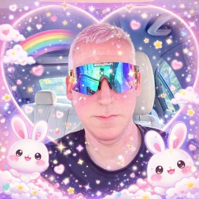 A selfie of a man wearing iridescent sunglasses with pink hair, decorated with a heart-shaped frame featuring rainbows, stars, sparkles, and cute white bunnies.