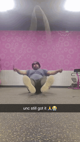 A blurry video clip of a man sitting on the floor doing crunches in a room with pink patterned wallpaper, with caption text reading 'unc still got it 🙏🔥'.