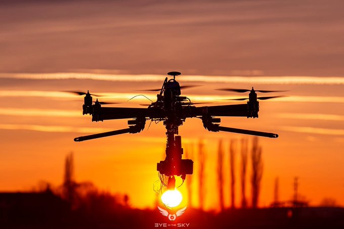 A silhouetted drone with extended arms and propellers hovers against a vivid orange sunset, with a 'SKY NET' logo visible at the bottom.
