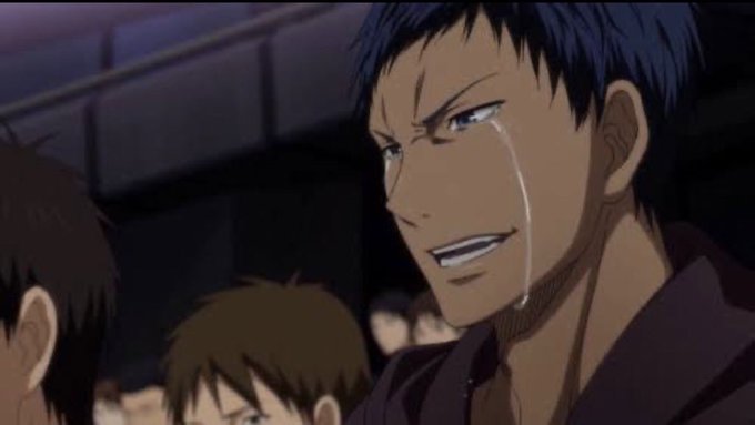 An anime screenshot of a dark-haired male character with tears on his face, appearing emotional in a crowded scene.