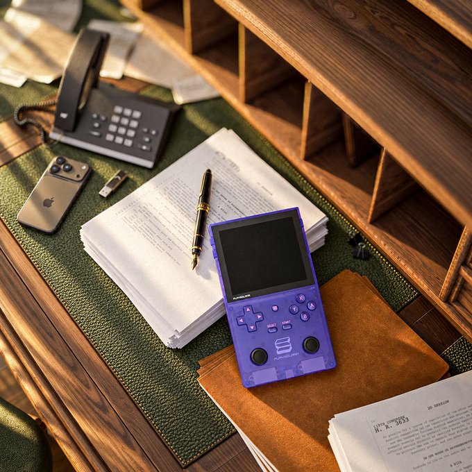 An overhead lifestyle photograph of a wooden desk with a purple translucent handheld gaming console, an iPhone, a pen, scattered papers, a telephone, and a brown leather notebook on a green textured mat.