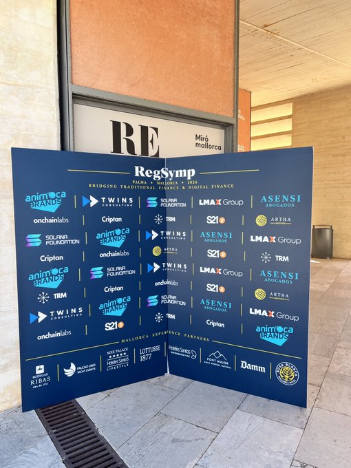 A sponsor backdrop for 'RegSymp Palma Mallorca 2026' displayed outside a building, featuring logos of partners including Animoca Brands, Twins, Solana Foundation, LMAX Group, Asensi Abogados, Tether, and Maltese Experience Partners.