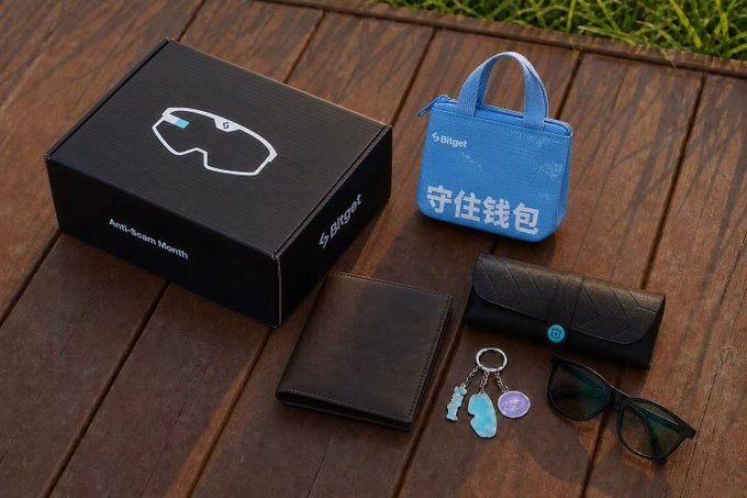 The image shows a wooden table with various items, including a wallet, sunglasses, a keychain, and a small blue bag. The wallet appears to have money tucked inside of it. There are also two pairs of sunglasses displayed on the table. A post on social media is shared in the image, which reads: "Huh? Could it be that the wallet I received also has money tucked inside it? I have to travel back to get the merchandise, pretty surprised that Bitget actually went out of their way to make special anti-fraud month merch @xiejiayinBitget @33Bitget Everyone remember to turn". The post seems to be related to a recent purchase or an interesting observation about the wallet.