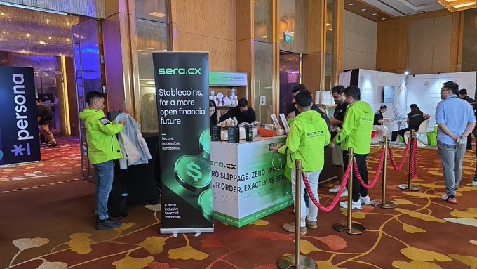 A conference booth for 'sera.cx' promoting 'Stablecoins, for a more open financial future' with text 'SECURE TRANSFERABLE BORDERLESS' and 'A more inclusive financial tomorrow,' staffed by people in green jackets.