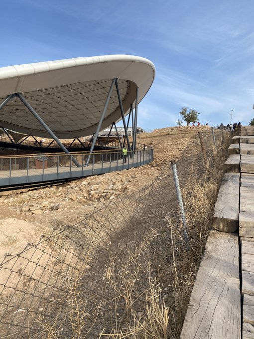 A futuristic white canopy structure with metal support beams overlooks a dry, fenced hillside landscape where visitors gather along a railing in the distance. The image's open, unconfined outdoor setting loosely mirrors the post's theme of sovereignty and user-controlled access, though no specific text, numbers, or names are visible in the scene.