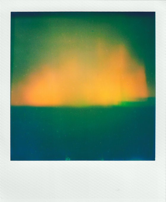An abstract, blurry polaroid-style image featuring glowing orange and yellow light fading into deep green and blue tones.
