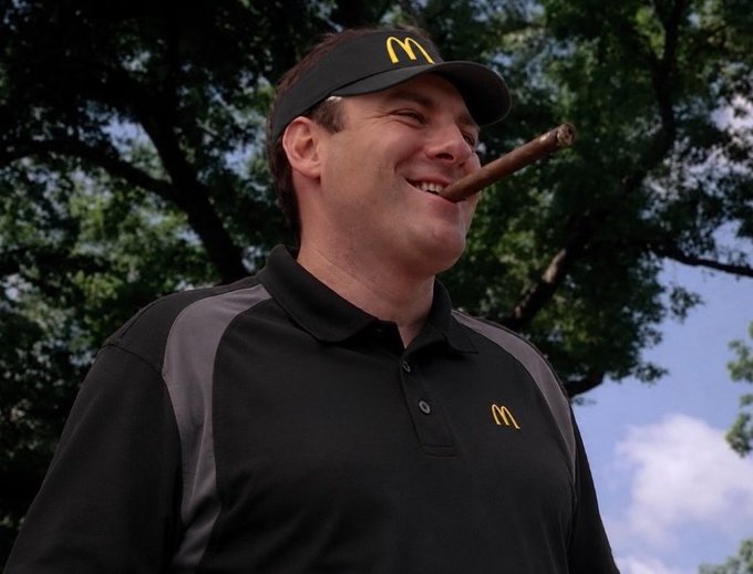 A man in a black McDonald's visor and polo shirt smiling while smoking a cigar outdoors.