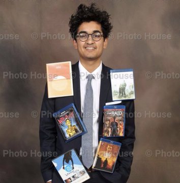 A smiling young man with curly dark hair and glasses poses in a suit and tie, holding up several video game cases including what appears to be "HERALD" and other titles, seemingly displaying new purchases following the sale of his memecoin positions.