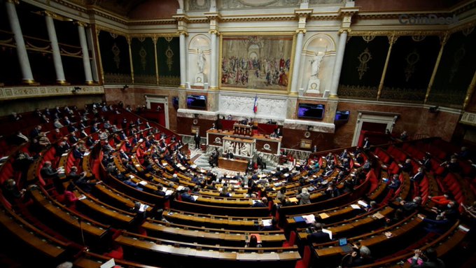 A wide interior view of the French National Assembly chamber filled with members during a session.
