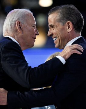 Two distinguished older men in dark suits share a warm embrace and smile at each other, with no visible text or identifying marks in the image. The accompanying post about Hunter Biden's $LAPTOP cryptocurrency token crashing 99.9% appears unrelated to the two men pictured, who bear no clear connection to the Biden family.