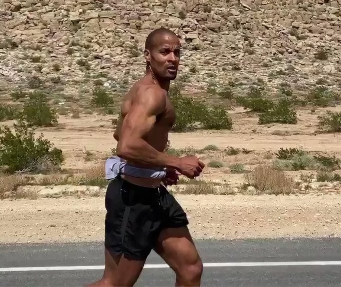 A shirtless, muscular man runs barefoot along a desert roadside, likely used as a humorous visual metaphor for "hiring a new Head of Stablecoins" — suggesting the Coinbase executive recruited someone who appears to be running away (or perhaps chasing) the job opportunity.