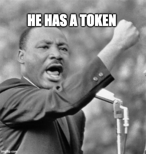 A black-and-white meme image of Martin Luther King Jr. speaking passionately at a podium, with the caption 'HE HAS A TOKEN' overlaid in bold white letters.