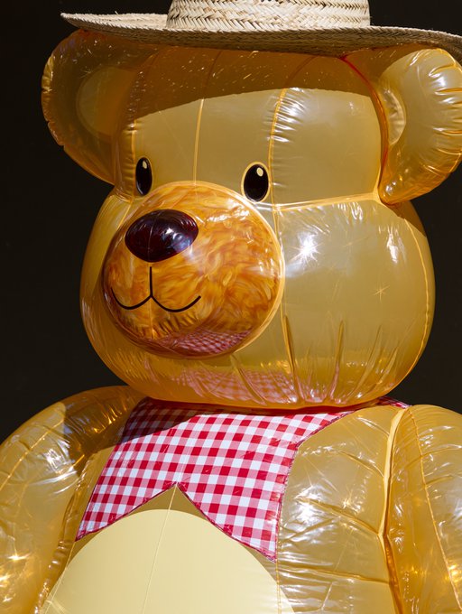 A large inflatable yellow teddy bear wearing a straw cowboy hat and a red and white checkered bandana.