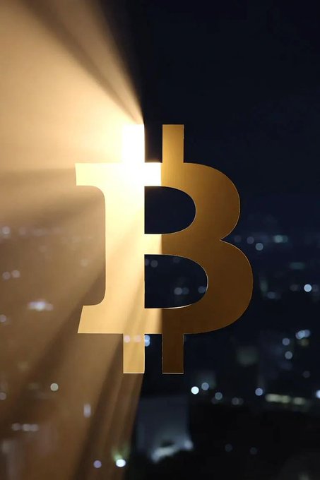 A golden Bitcoin (₿) symbol glows brightly with light rays emanating from behind it against a dark, blurred cityscape background.
