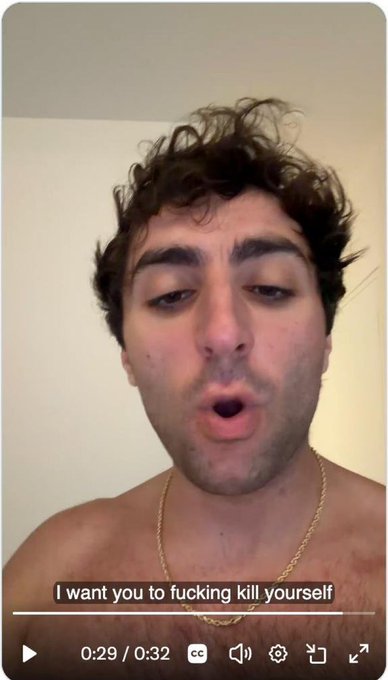 A shirtless man with curly hair wearing a gold chain makes an "O" shape with his mouth in a selfie-style video, with the caption "I want you to fucking kill yourself" displayed on screen; the video timestamp reads 0:29/0:32.