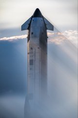 A dramatic image of a space shuttle ascending through clouds with its rocket boosters glowing brightly against a hazy sky.