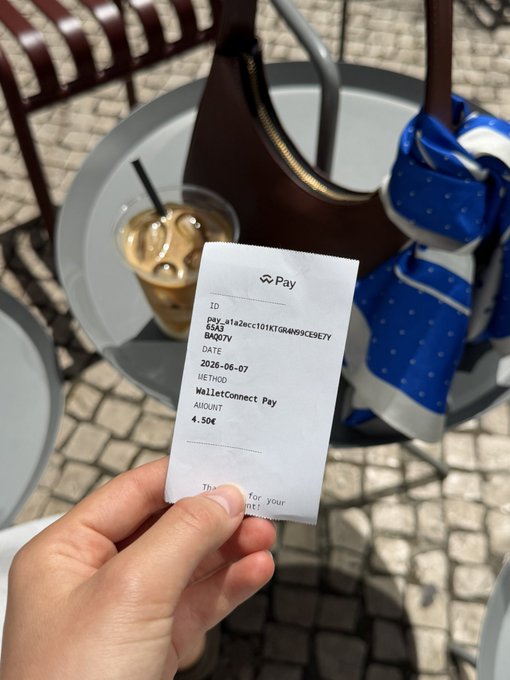 A hand holds a 'Pay' receipt dated '2026-06-07' showing a 'WalletConnect Pay' payment of '4.50€', with an iced coffee and brown bag on a table in the background.