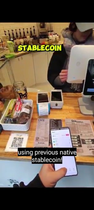 A customer uses their smartphone to scan a café's payment terminal, with the caption "STABLECOIN" and "using previous native stablecoin!" overlaid, illustrating the post's message about seamless crypto adoption as the user pays via satUSD in a real-world setting.
