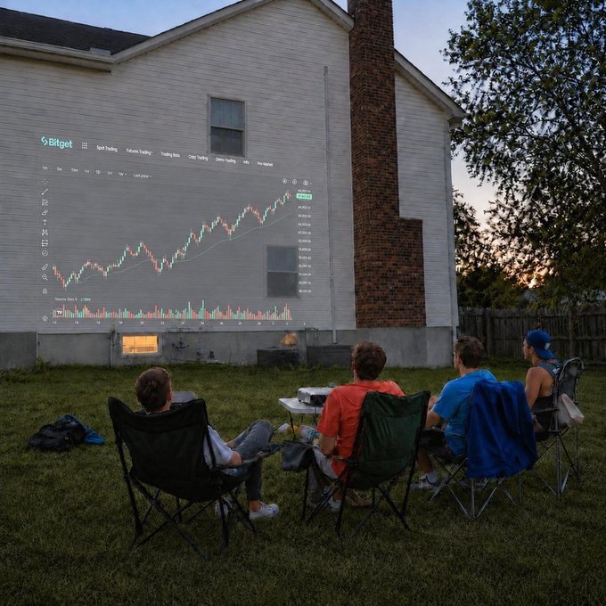 A group of four people sit in folding chairs on a lawn at dusk, watching a projected Bitget trading chart on the side of a white house, showing stock price data including Volume, RSI, and MA lines.