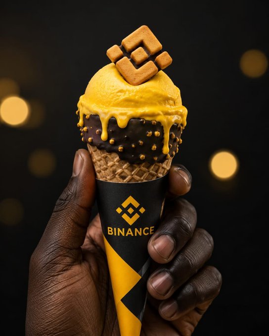 A hand holds a luxurious ice cream cone featuring a scoop of yellow ice cream drizzled with chocolate and topped with a Binance logo-shaped cookie. The cone's wrapper prominently displays the "BINANCE" branding alongside its diamond logo, tying into the "gm!" (good morning) greeting often used in crypto communities as a friendly daily check-in.