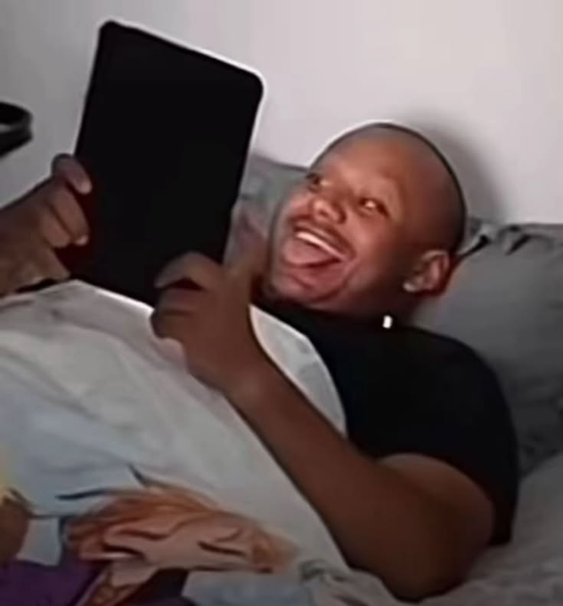A meme image showing a man laughing excitedly while holding a tablet in bed.