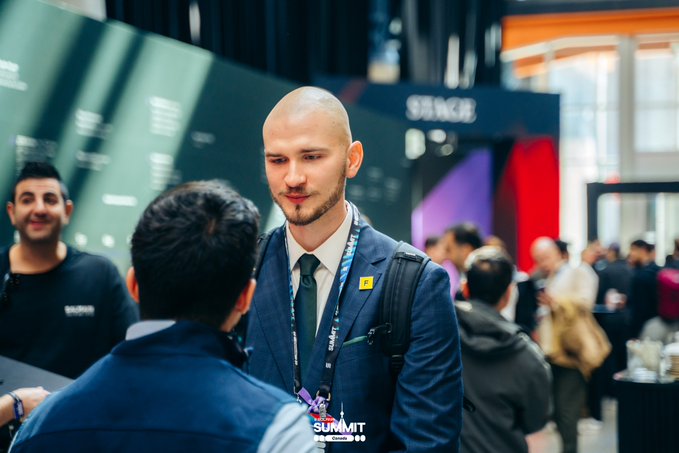 A bald man with a beard in a blue suit and tie speaks with someone at an event, with a 'Web Summit' lanyard visible.