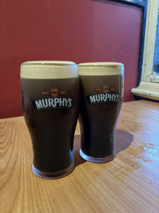 Two pints of Murphy's Irish stout sit side by side on a wooden table against a red wall, fitting the "Beers" caption with their creamy heads and matching branded glasses.
