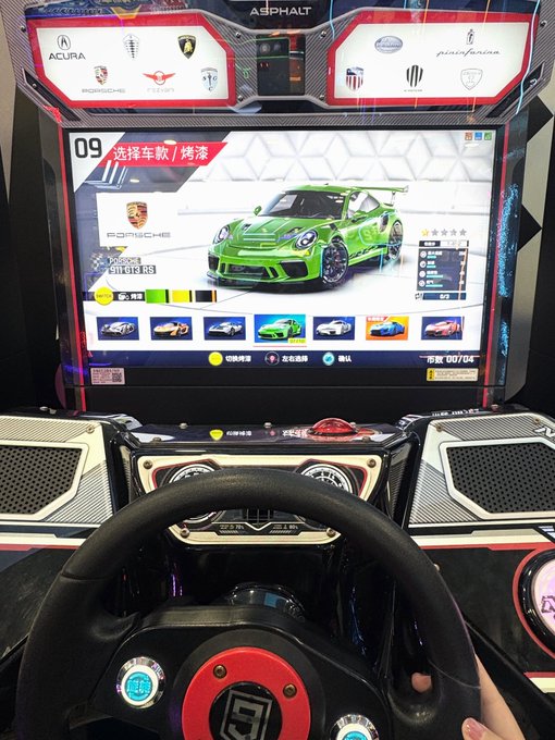 A person playing an arcade racing game, with a green Porsche 911 GT3 RS displayed on the screen featuring "ASPHALT" branding and a "选择车款/烤漆" (Select Car/Paint) menu.