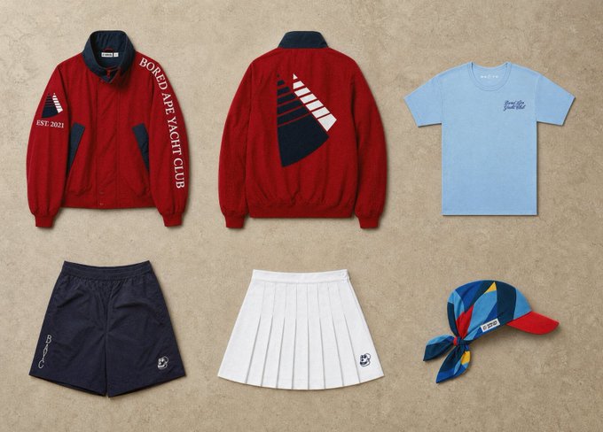 A flat-lay product display featuring a red Bored Ape Yacht Club jacket, a light blue t-shirt, black shorts, a white pleated skirt, and a blue patterned headscarf.