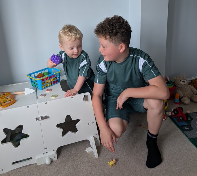 A father kneels on the floor playing with his two young sons among scattered toys, reflecting the post's heartfelt message that everything he does is for his beautiful boys.