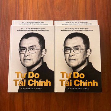 Two copies of the Vietnamese edition of "Tự Do Tài Chính" by Changpeng Zhao (CZ) are displayed side by side on a wooden surface, featuring his portrait on the cover and the text "ĐÓ LÀ SỰ VIỆC ĐƠN GIẢN" (the statement about banking financial inclusion for the unbanked). The image previews the Vietnamese translation of CZ's book, aligning with the post's excitement about its local availability and hinting at a potential future book launch event in Vietnam with @cz_binance.