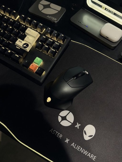 Gaming setup featuring an ASTER x Alienware mousepad with matching branded mouse, alongside a mechanical keyboard with custom keycaps, a stream deck, and a phone stand, all branded with the ASTER and Alienware logos.