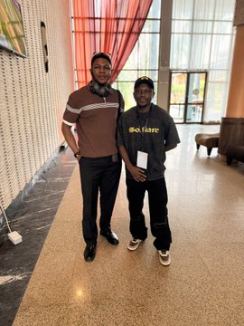 Two men pose for a photo indoors, one wearing a brown polo shirt and the other wearing a gray 'GoVans' branded shirt.