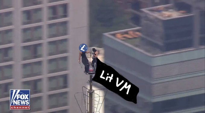 A person climbs atop a flagpole between tall city buildings on Fox News, with a digitally added black banner displaying the text "Lit VM" overlaid on the scene.