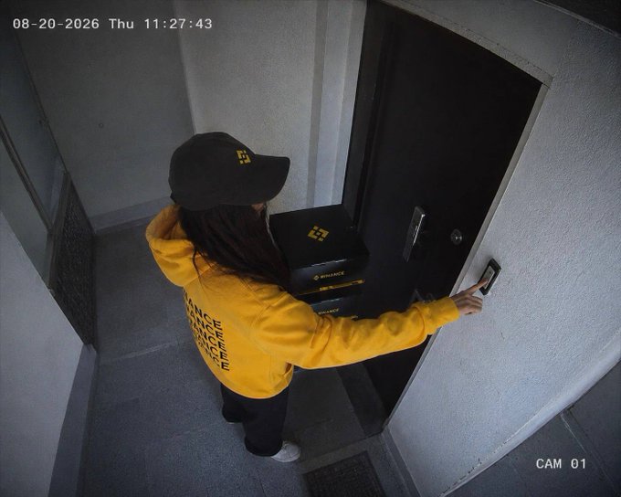 Surveillance camera footage (CAM 01, timestamp 08-20-2026 11:27:43) shows a delivery worker wearing a yellow Binance hoodie and cap ringing a doorbell while holding a package.