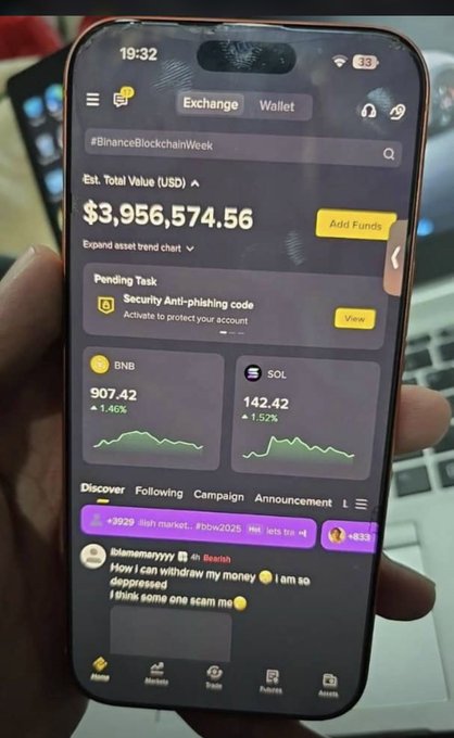 A person holding an iPhone displaying a Binance app screen with an estimated total crypto value of $3,956,574.56, showing BNB at 907.42 (+1.46%) and SOL at 142.42 (+1.52%), with a 'Security Anti-phishing code' pending task.