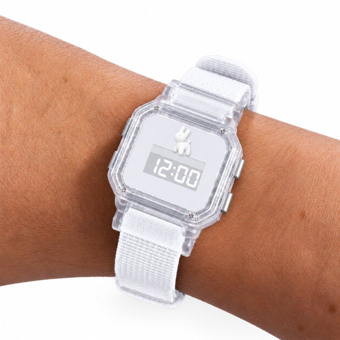 A wrist wearing a clear digital watch with a white fabric strap, displaying the time 12:00 and featuring a small white dog figurine on the screen.