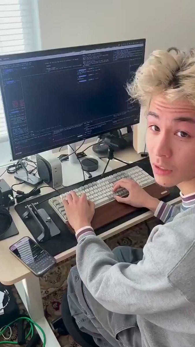 The image features a young man sitting at a desk with a computer monitor, keyboard, mouse, and cell phone. He appears to be working or studying, possibly using an AI-powered decision engine for trading purposes. The scene suggests that he is engaged in a project related to artificial intelligence, as the AI system has been integrated into his daily routine to help him make decisions more efficiently.
