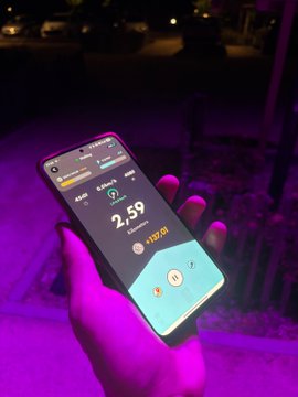 The image shows a person holding up their phone, which displays a fitness tracking app that tracks steps taken during an evening walk. The app provides information about the distance walked, calories burned, and time spent walking. The person's hand is visible on the right side of the frame, while the phone is held in the left corner.