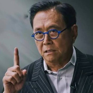 An older Asian man with blue round glasses wearing a pinstripe suit and white shirt raises his index finger while speaking.