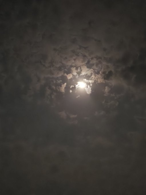 The image shows a beautiful night sky with a bright full moon shining through the clouds. The moon appears as a large, glowing orb against the dark backdrop of the cloudy sky. The photo has been captioned with various phrases such as "Good night CT," "Today is hot day," and "@NomismaNetwork" to provide context about the image's content or the creator behind it.