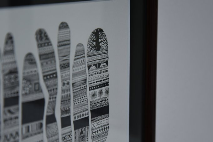 A close-up, angled photograph of a framed black and white artwork depicting five elongated fingers filled with intricate decorative patterns and motifs.