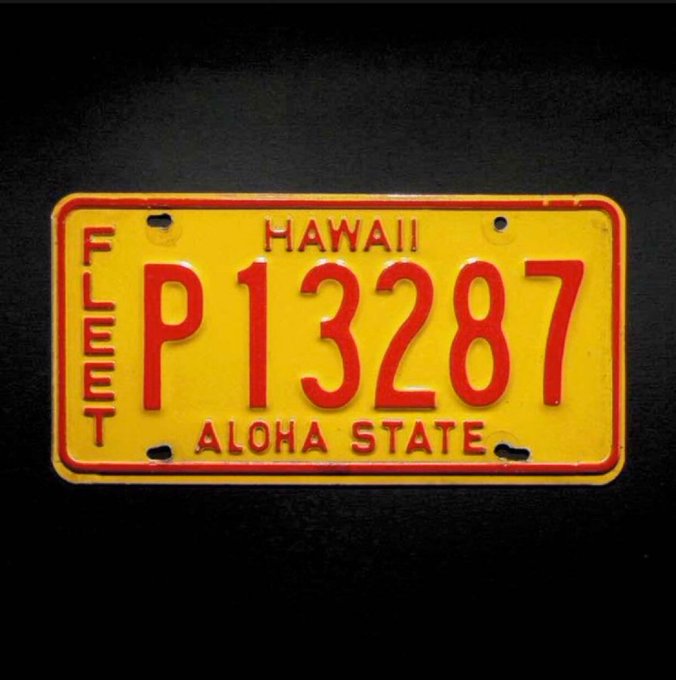 A vintage yellow and red Hawaii license plate reads 'FLEET P13287' with 'HAWAII' at the top and 'ALOHA STATE' at the bottom, displayed against a black background.